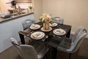 Comedor con una mesa negra dispuesta para cuatro personas, rodeada de sillas estampadas.