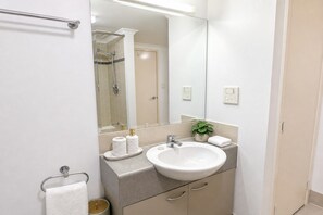 Un baño con un lavamanos blanco, un espejo, un perchero para toallas y una planta pequeña.