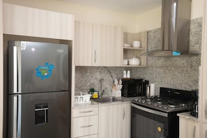 A modern kitchen with a stainless steel refrigerator, a gas stove, and granite countertops. - NOK Cozy 2BR Stay in Vistacana Punta Cana (Punta Cana)