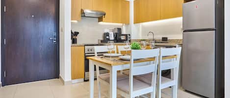 A modern kitchen with wooden cabinets, a stainless steel refrigerator, and a dining table set for two.