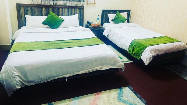 Habitación de hotel con dos camas, una mesita de noche, una botella de agua y una alfombra estampada.