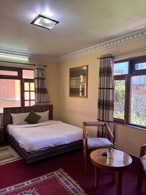 Un dormitorio con cama, una silla, una mesa y un ventanal con cortinas.