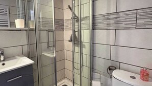 A bathroom with a glass-enclosed shower, a sink, and a toilet. - Cozy Seafront Studio on the Mediterranean (Agde)