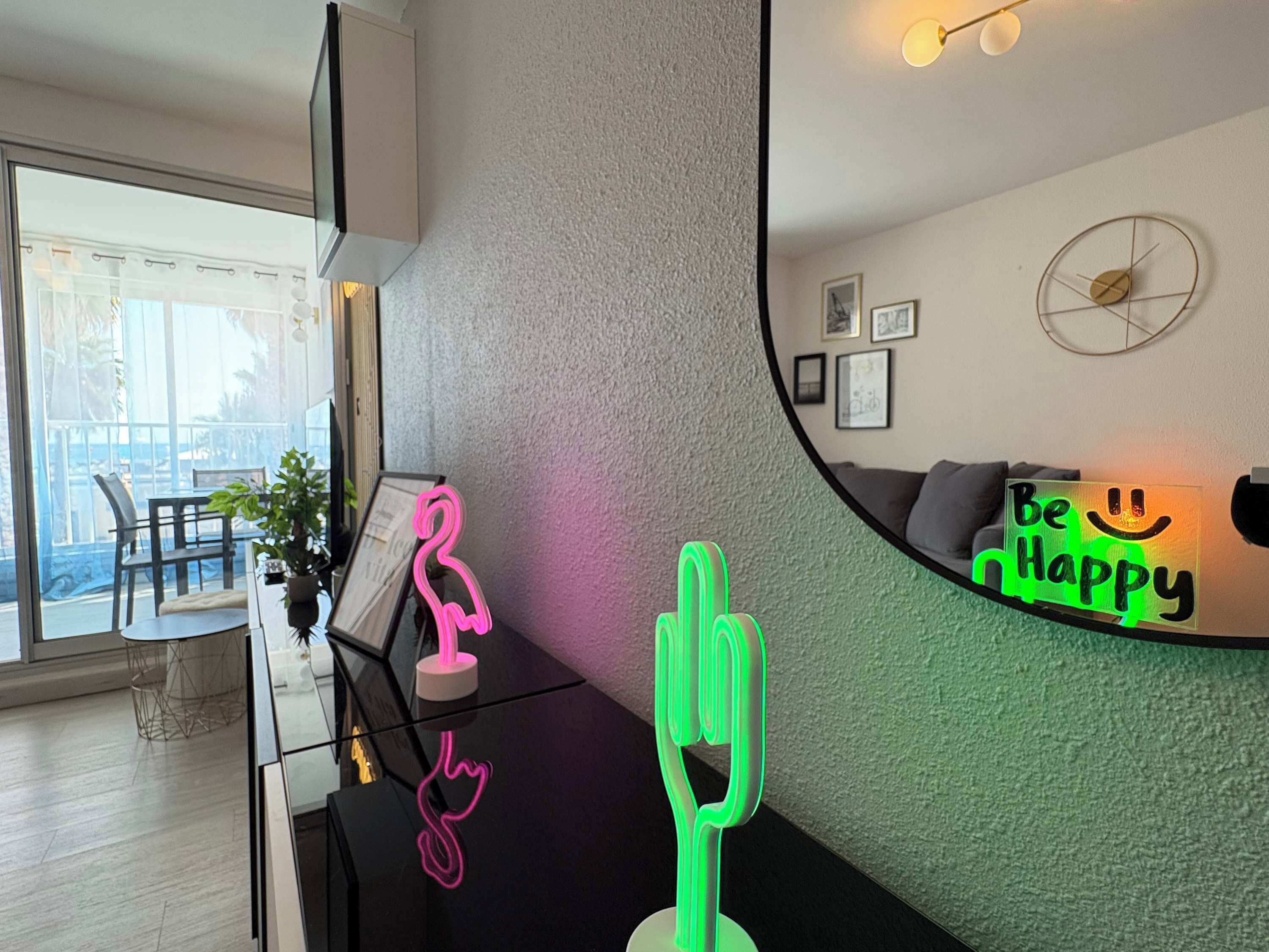 Een moderne woonkamer met een glazen salontafel, een spiegel die de kamer weerspiegelt, en een neonbord aan de muur.
