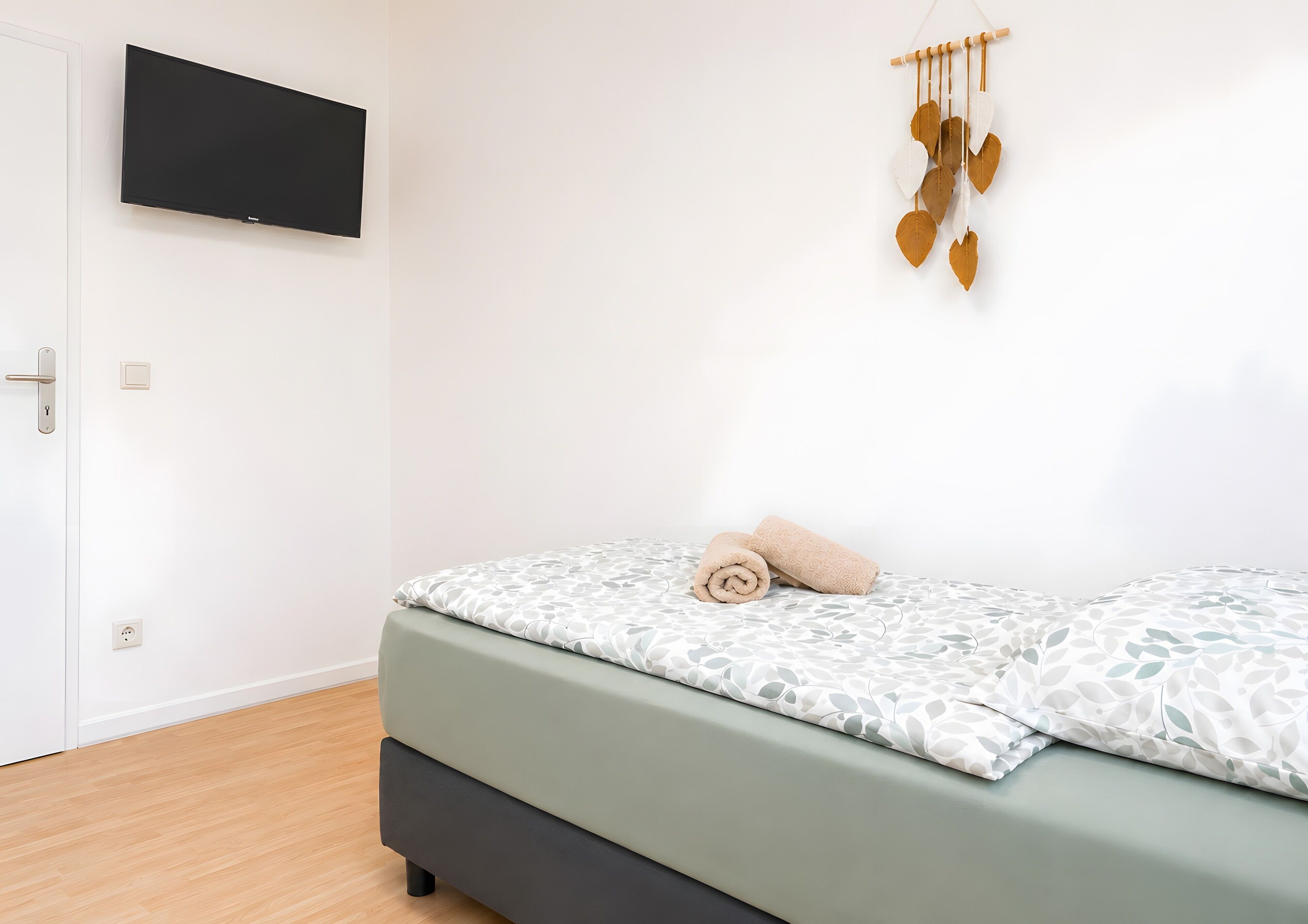 A bedroom with a bed, a wall-mounted TV, a door, and a wall decoration.