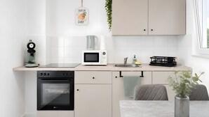 Una cocina moderna con horno integrado, microondas y cafetera. Hay una mesa de comedor con un jarrón y una silla.
