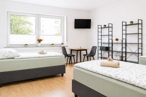 Une chambre d’hôtel avec deux lits, une télévision, un bureau, des chaises et une fenêtre donnant sur des arbres.