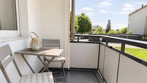Un balcón con mesa y sillas, y vista al vecindario, con barandilla.