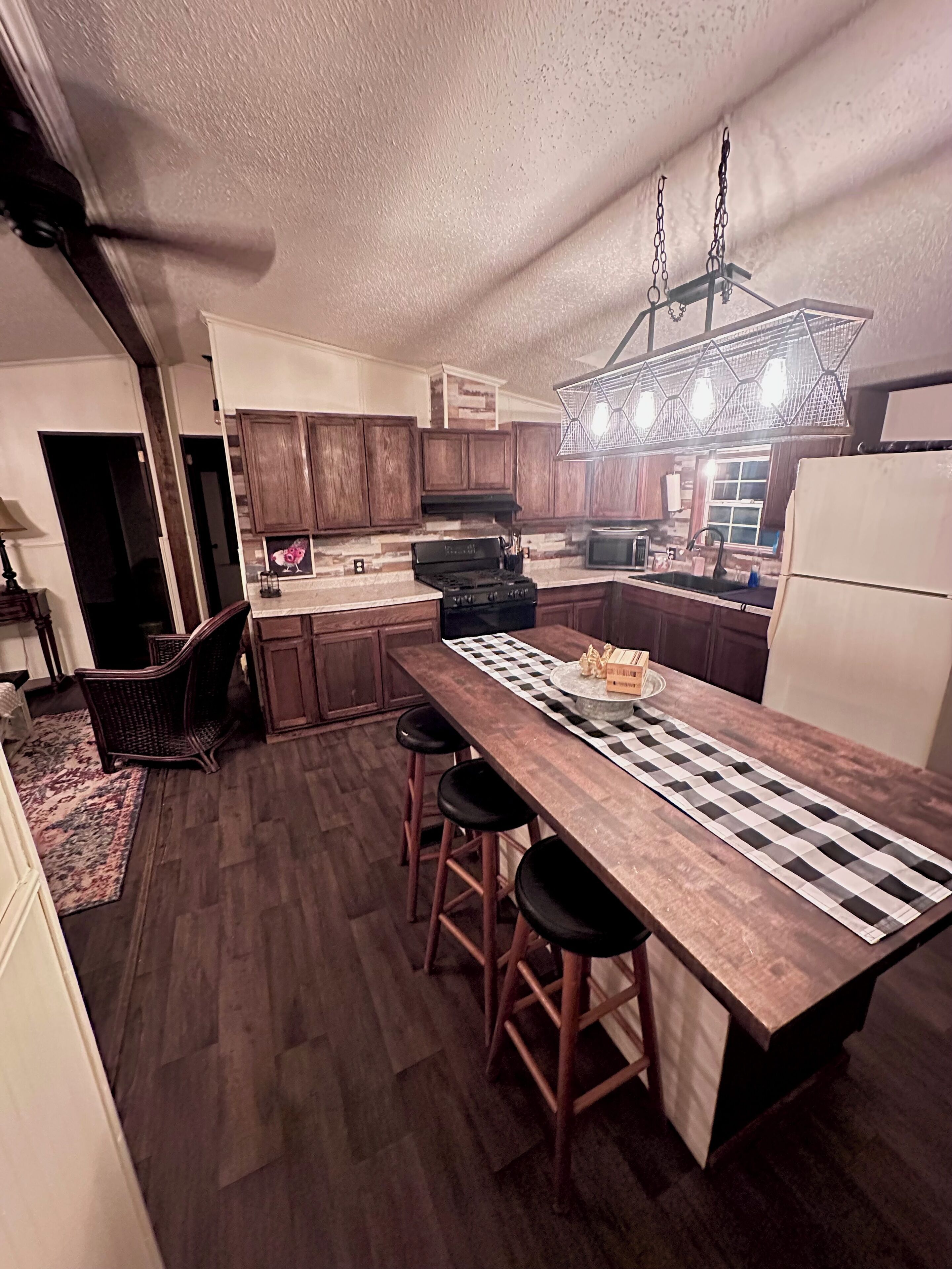 Una cocina moderna con armarios de madera, una isla central con taburetes, estufa integrada y una lámpara colgante.