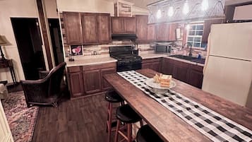 Una cocina moderna con armarios de madera, una isla central con taburetes, estufa integrada y una lámpara colgante.