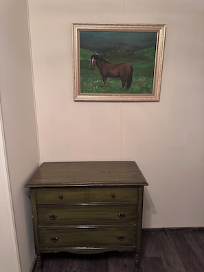 A green dresser with three drawers against a wall with a framed painting of a horse.