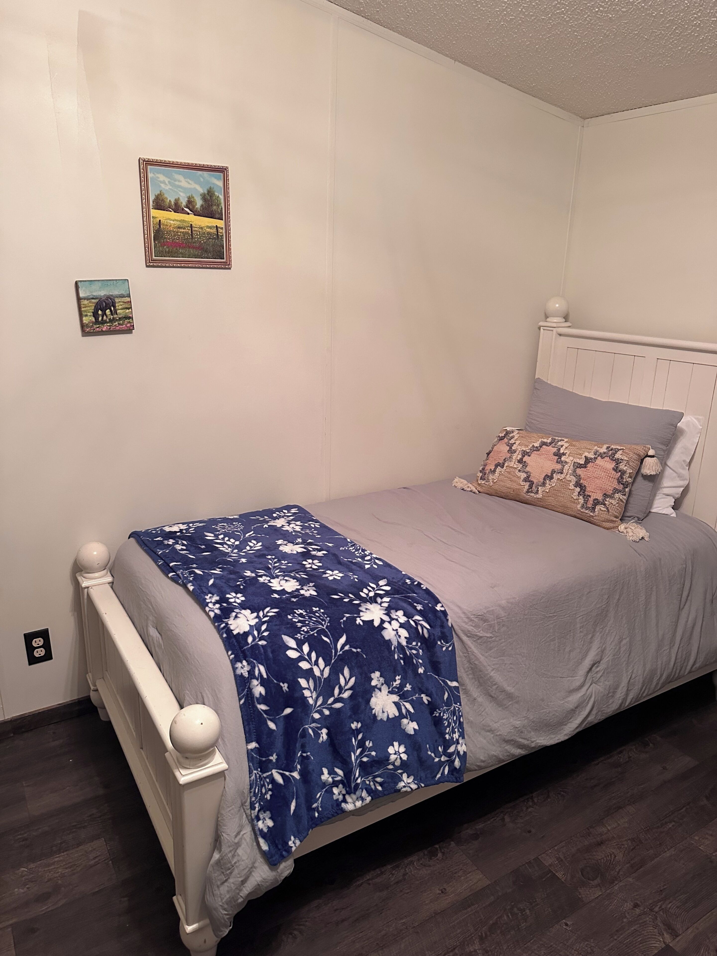 Un letto singolo con una testiera bianca, una coperta a fiori blu e due cuscini.