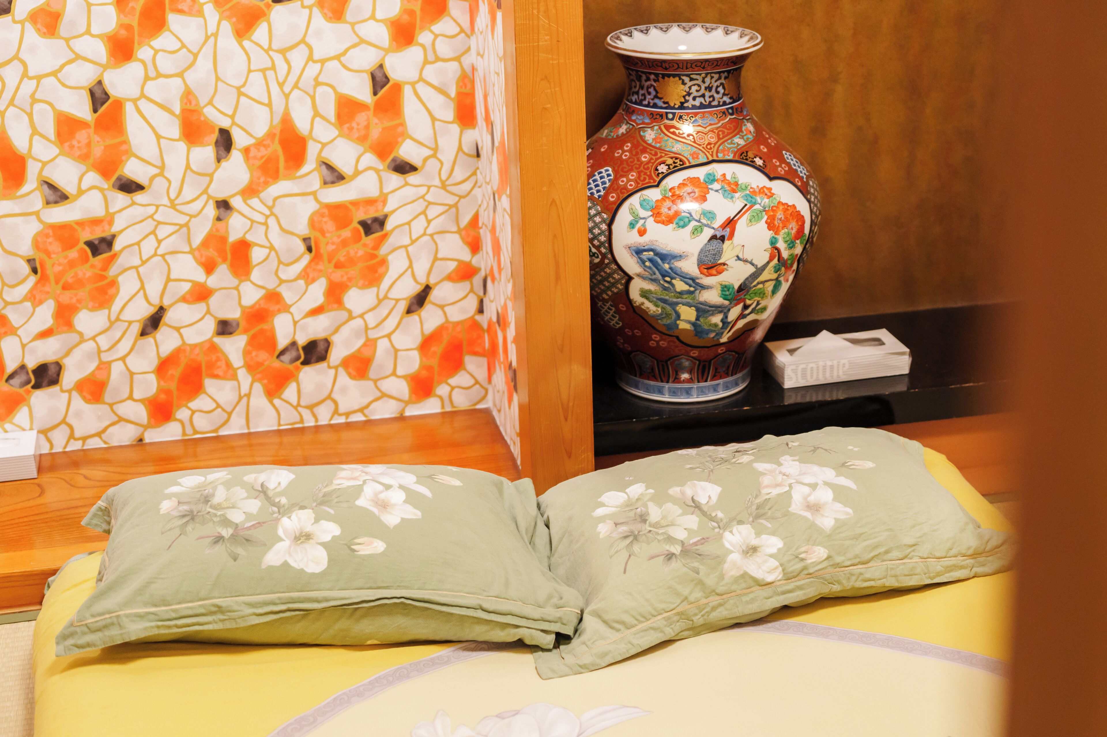 Una cama con almohadas florales, un jarrón decorativo y una pared de mosaico.