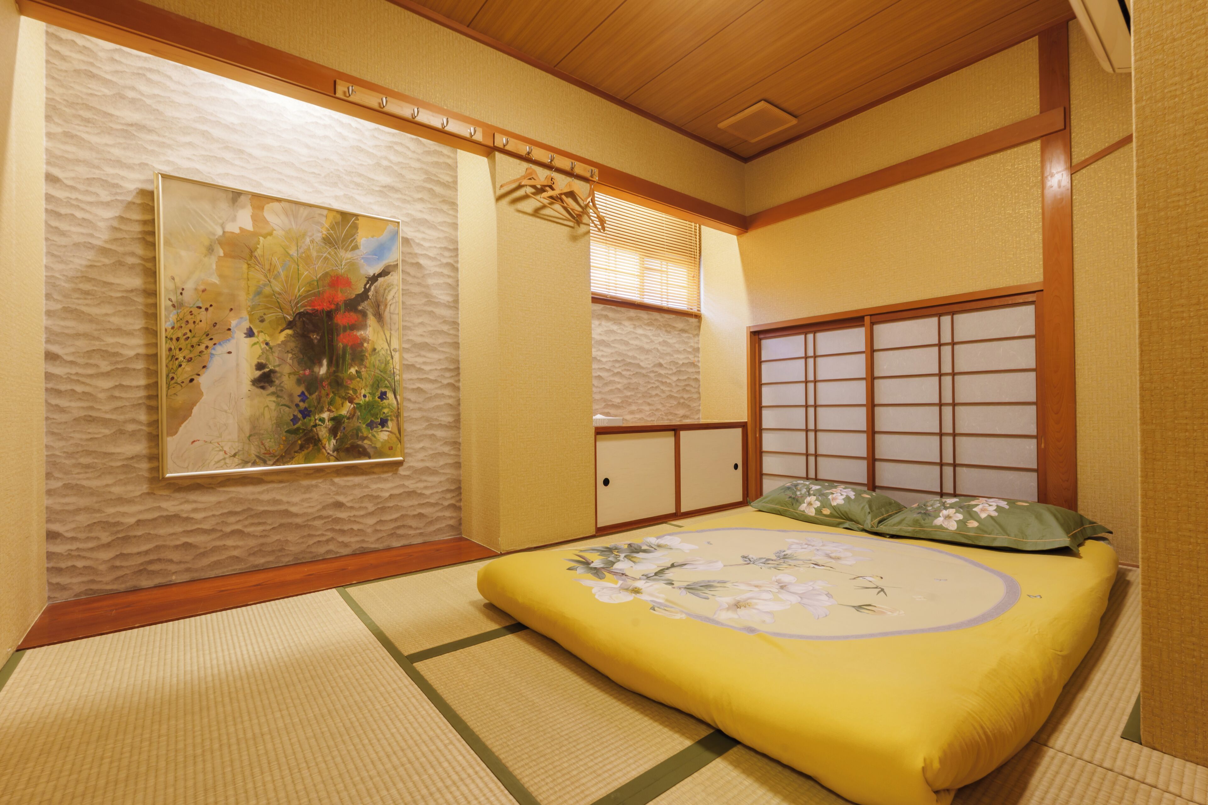A traditional Japanese-style room with tatami flooring, a low bed with floral bedding, a shoji screen, and a painting on the wall.
