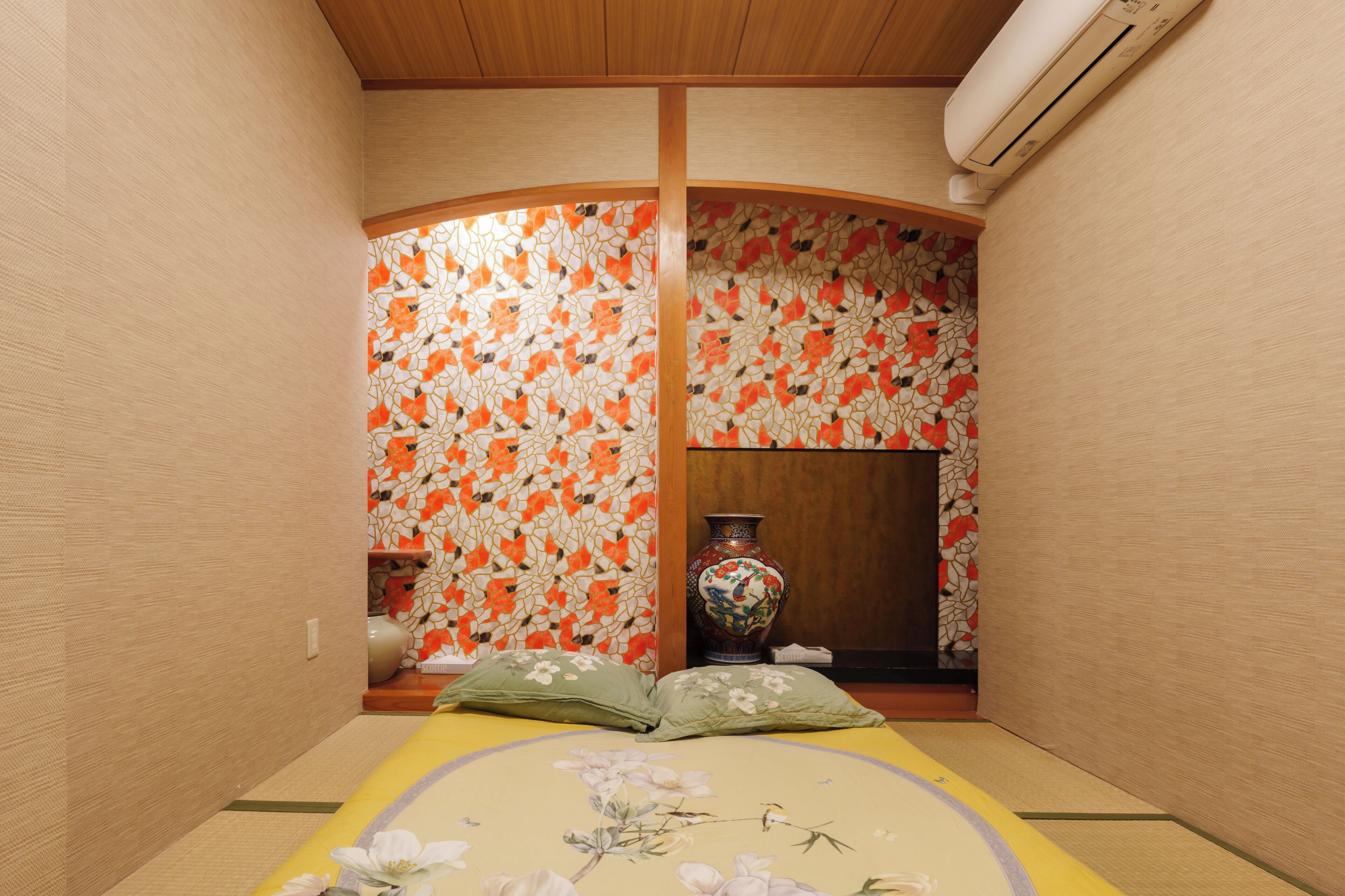 A traditional Japanese room with tatami flooring, a low wooden ceiling, and a curved wall with a mosaic pattern.