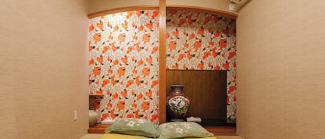A traditional Japanese room with tatami flooring, a low wooden ceiling, and a curved wall with a mosaic pattern.