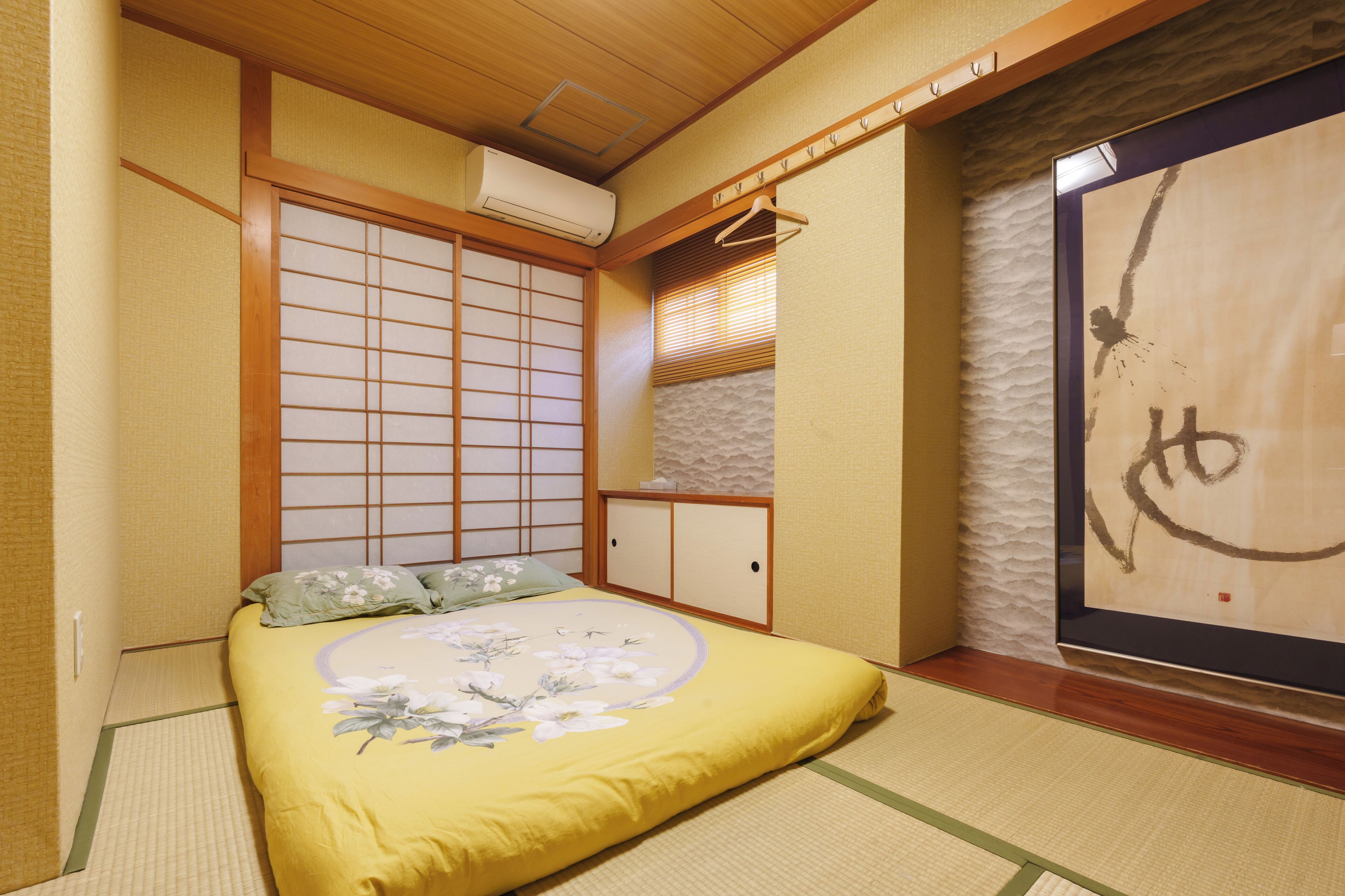 Een traditionele Japanse kamer met tatami vloeren, een laag bed met bloemenbedrukking, een shoji-scherm en een schuifdeur.
