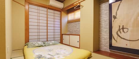 A traditional Japanese-style room with tatami flooring, a low bed with floral bedding, a shoji screen, and a sliding door.