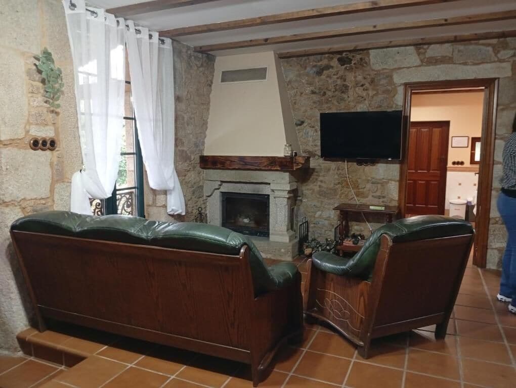 A living room with a stone wall, a fireplace, a television, and two leather sofas.