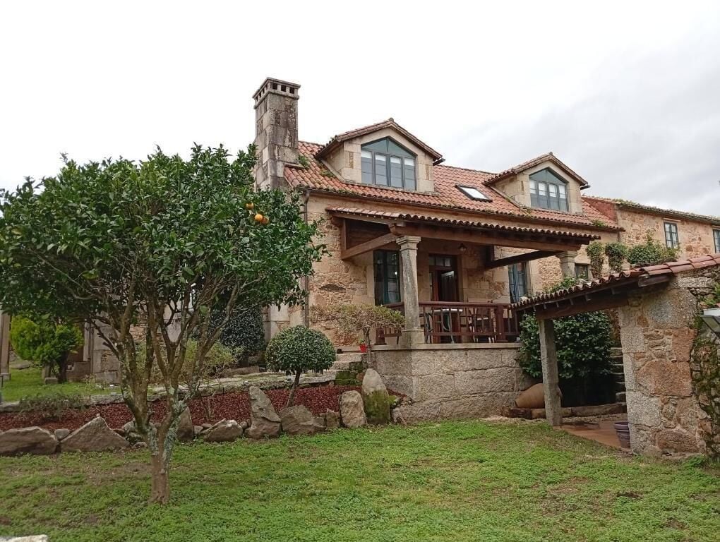 A stone house with a tiled roof, a covered porch, and a well-maintained garden.