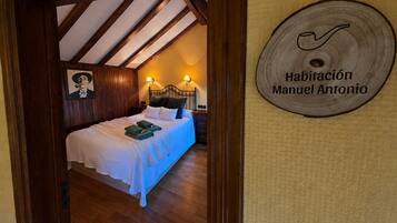 A bedroom with a wooden ceiling, a bed with white bedding, and a wall-mounted sign reading 'Habitación Manuel Antonio'.