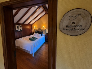Un dormitorio con techo de madera, una cama con ropa de cama blanca y un letrero en la pared que dice 'Habitación Manuel Antonio'.