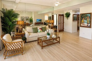A spacious living room with a sofa, coffee table, and wicker chairs. There are potted plants and artwork on the walls. - Kapalua Ridge | 2 Ocean View Villas, Sleeps 12 | Car Incl. w/ 6+ Nights | ML-4253 by KBM (Lahaina)