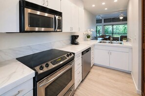 A modern kitchen with a built-in microwave, stove, and dishwasher, white cabinetry, and a view of the outdoors. - Kapalua Ridge | 2 Ocean View Villas, Sleeps 12 | Car Incl. w/ 6+ Nights | ML-4253 by KBM (Lahaina)
