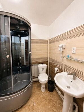 A bathroom with a glass-enclosed shower, a toilet, and a sink. - Grand Sky Hotel (Almaty)