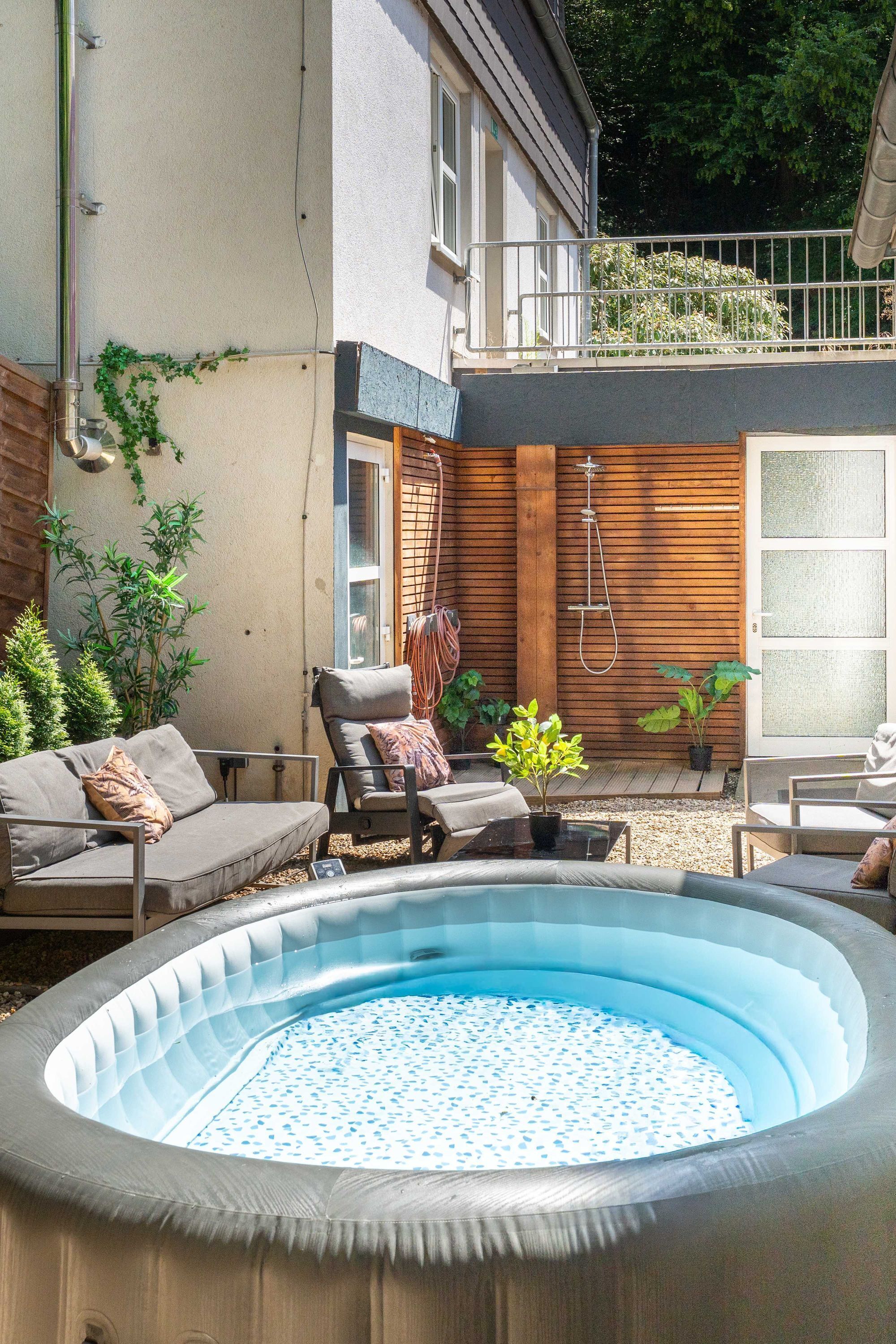 Una piscina exterior con un deck de madera, sillas de descanso y una pequeña zona ajardinada.
