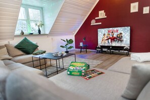 A cozy living room with a sofa, a coffee table, a TV displaying a Netflix show, and a plant.