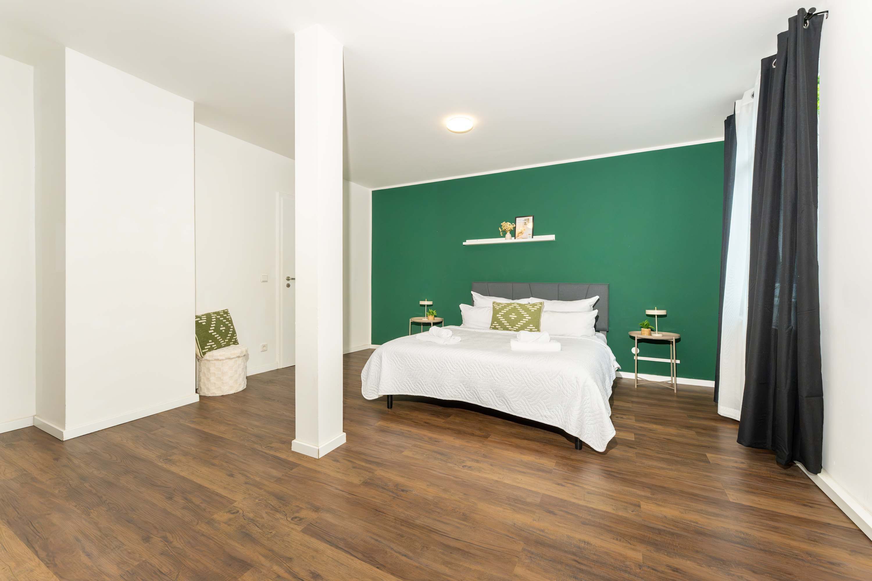 A bedroom with a bed, a nightstand, a wall-mounted shelf, and a potted plant.