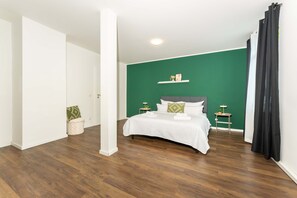 A bedroom with a bed, a nightstand, a wall-mounted shelf, and a potted plant.