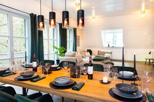 Un comedor con mesa de madera dispuesta para una comida, rodeada de sillas, con una decoración moderna y ventanas amplias.