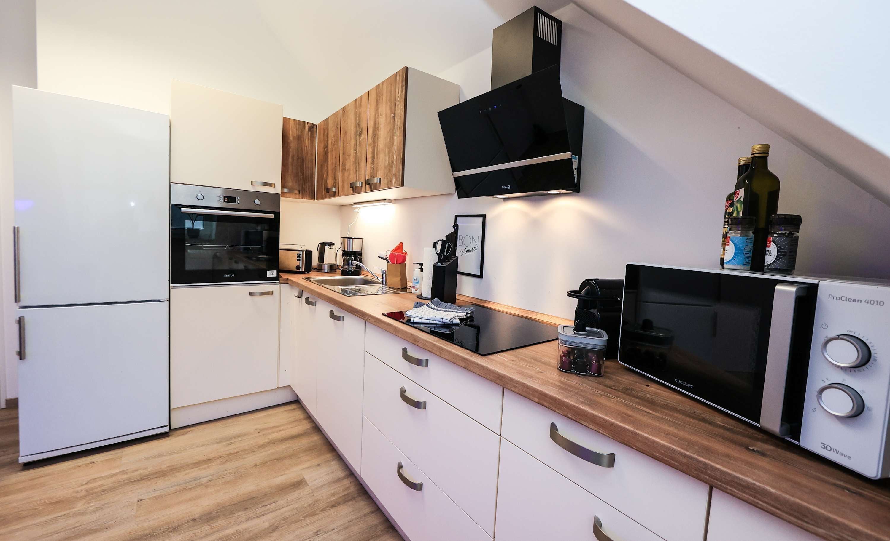 A modern kitchen with white cabinets, a wooden countertop, a built-in oven, a coffee maker, and a ProClean 4010 dishwasher.