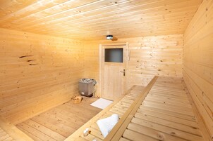 Pequeña sauna de madera con puerta, banco y calentador.