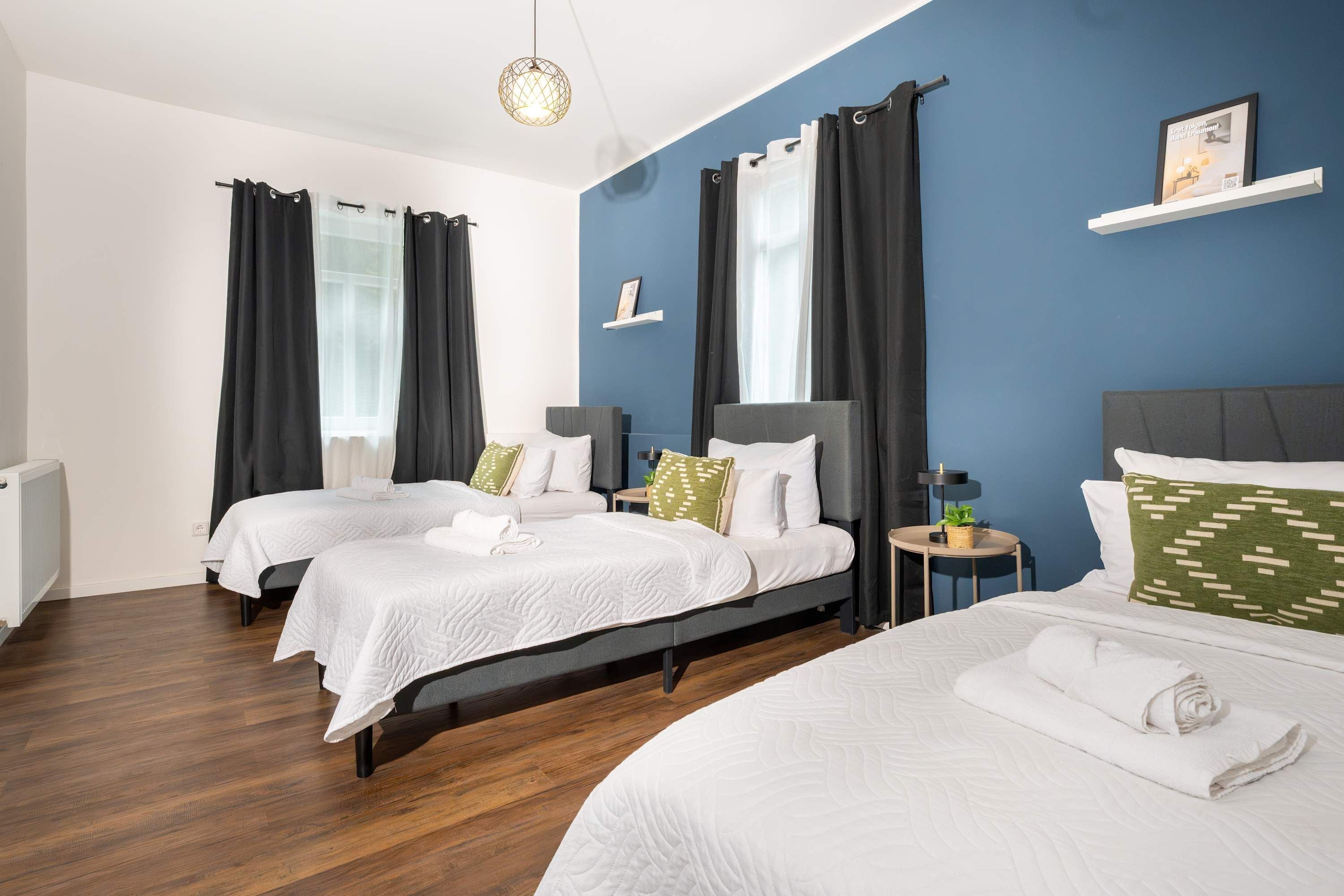 Ein Hotelzimmer mit zwei Betten, einem kleinen Tisch, einem Nachttisch, einer Wandablage und einer Heizung.