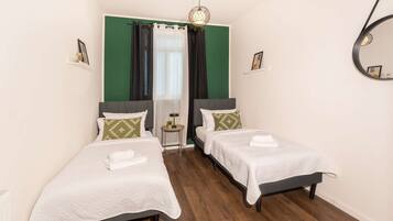 A hotel room with two single beds, a small table, a mirror, and a green accent wall.