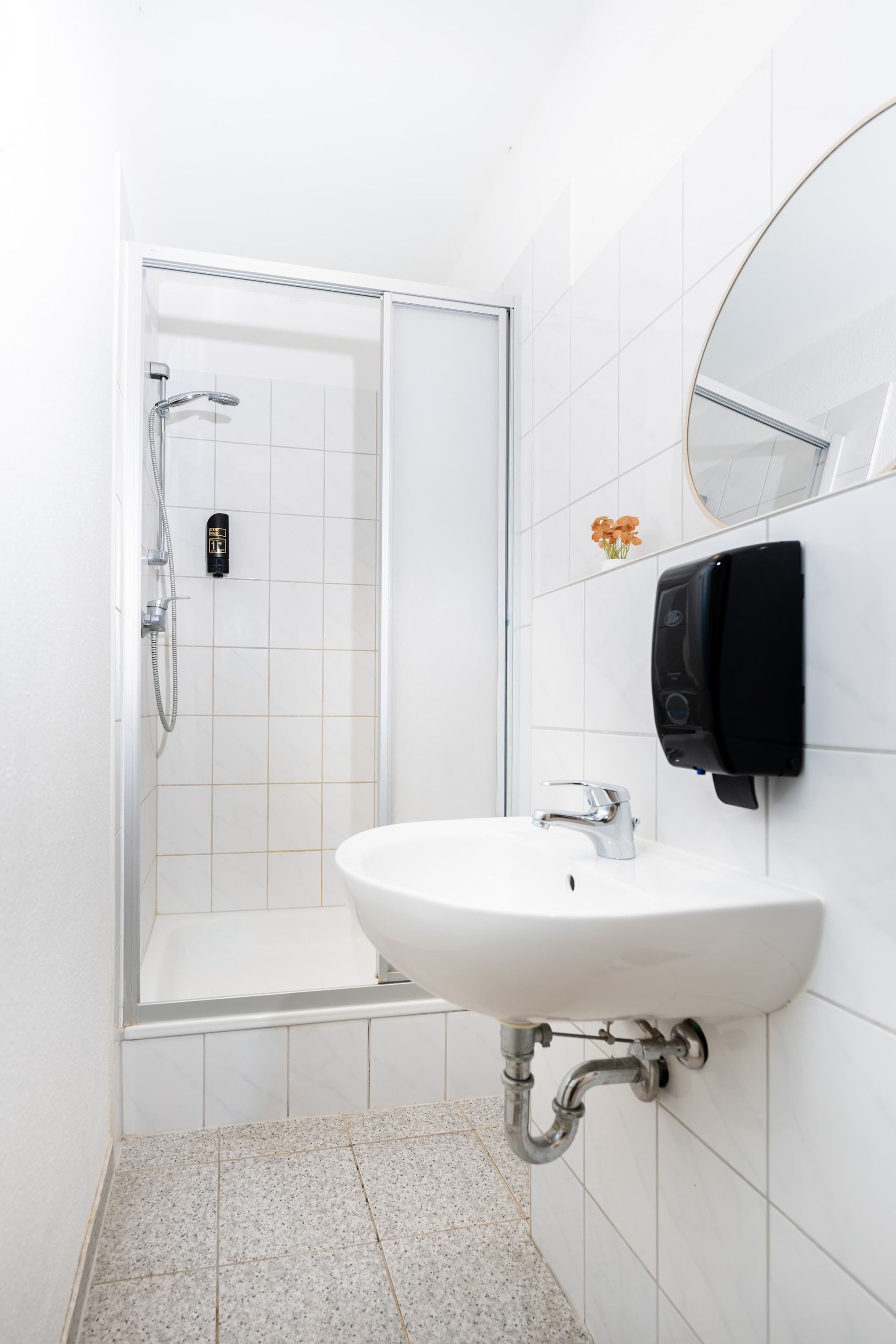 Un baño con lavamanos blanco, ducha de mano y teléfono instalado en la pared.