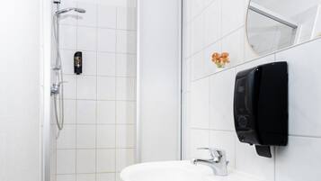 Un baño con lavamanos blanco, ducha de mano y teléfono instalado en la pared.