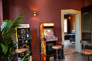 A room with two arcade machines, a plant, and a view into another room with a pool table.