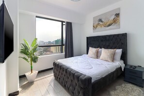 A modern bedroom with a large bed, a potted plant, a city view, and a mounted artwork. - Staroot - The City Elegance  (Nairobi)