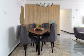 A modern dining area with a wooden slat partition, a round table, and six grey upholstered chairs.
