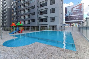 Ein Schwimmbecken mit Fliesen umgeben von einem Hochhaus mit mehreren Balkonen.