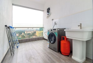 A laundry room with a washing machine, a gas cylinder, a sink, and a view of a cityscape through a large window.