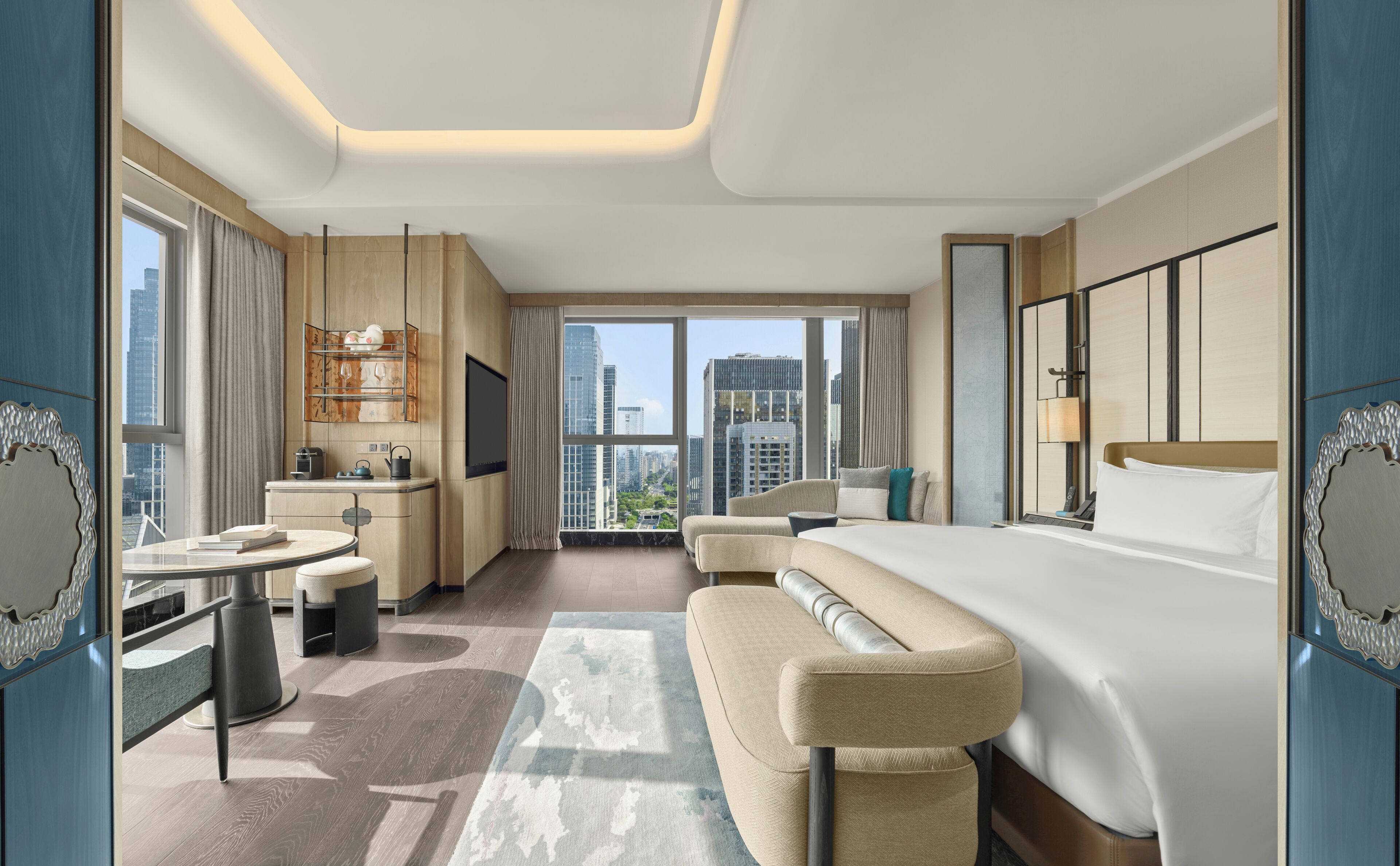 Habitación de hotel moderna con una cama grande, un sofá, un escritorio con silla y vistas a la ciudad a través de las ventanas.