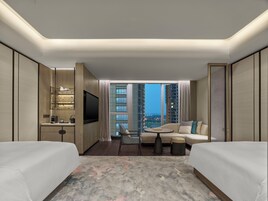 A hotel room with a large window, a flat-screen TV, a sofa, a coffee table, and two beds.