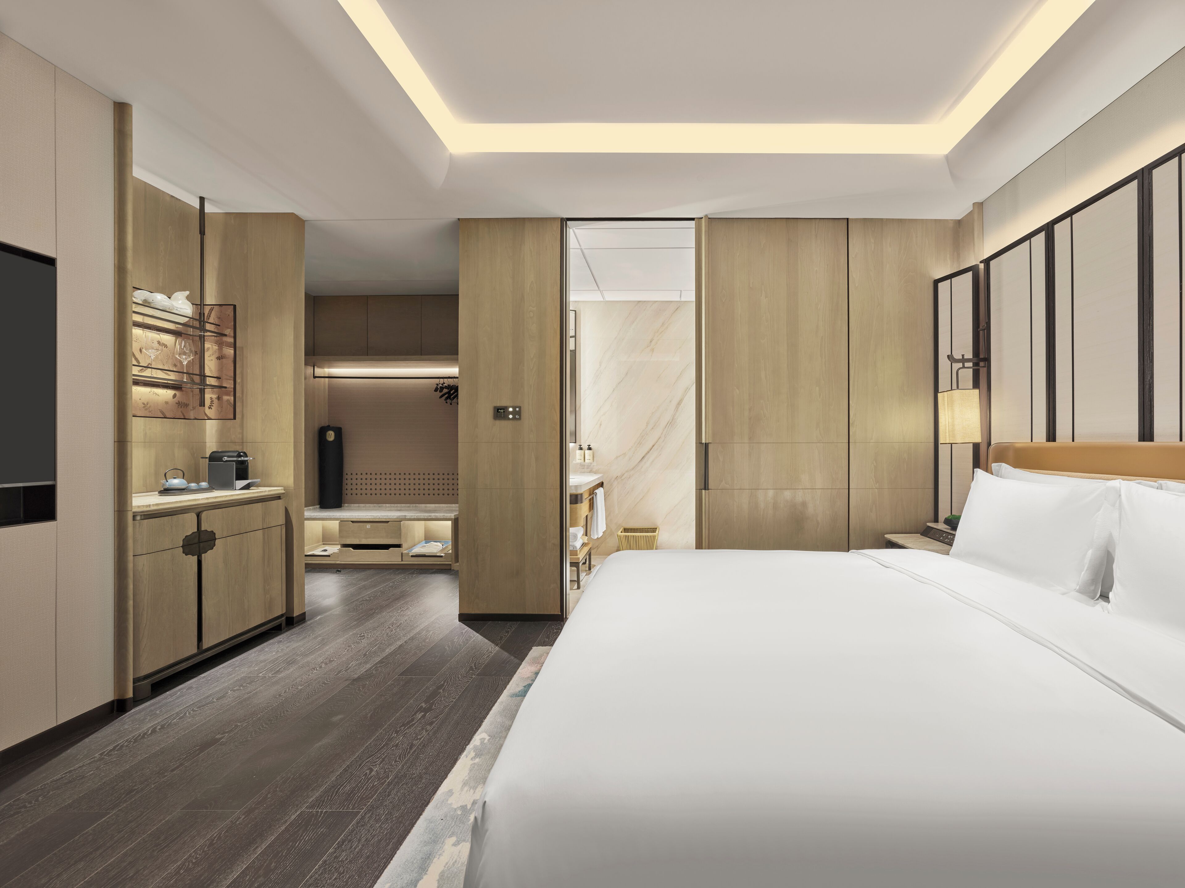 A modern hotel room with a large bed, a flat-screen TV, a desk with a chair, and a wardrobe.