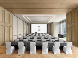 A conference room with a large screen, rows of tables, and chairs.