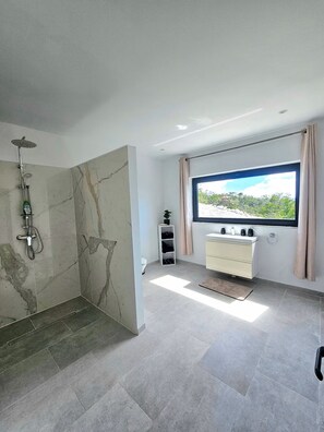 Un baño moderno con ducha, tocador con lavamanos y un amplio ventanal con vistas.